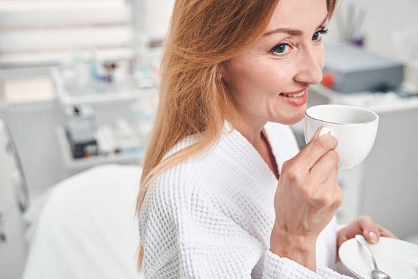 Jolly woman with coffee in beauty clinic - 写真・画像