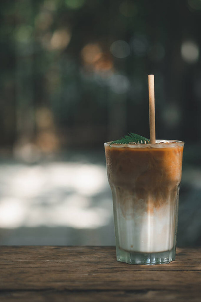 Refreshing iced latte coffee in a glass with paper straws in an outdoor cafe background - Zdjęcie, obraz