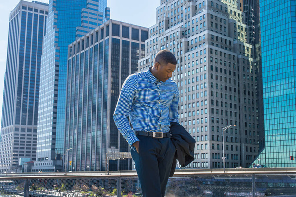 Un joven hombre de negocios negro está parado en un distrito de negocios, mirando hacia abajo y pensando profundamente - Foto, Imagen