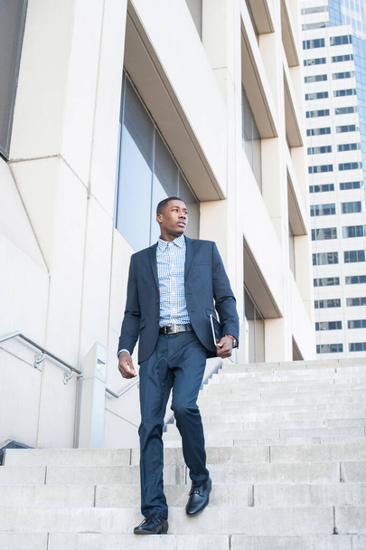 Ένας νεαρός όμορφος μαύρος επιχειρηματίας κατεβαίνει βήματα από ένα κτίριο επιχειρήσεων. - Φωτογραφία, εικόνα