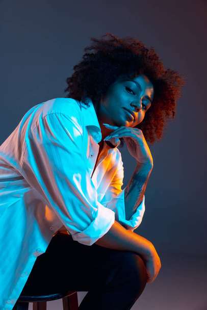 Full-length portrait of African young girl casual clothes, outfit isolated on dark blue studio background in pink neon light. Concept of human emotions, facial expression, youth, sales, ad. - Foto, Imagem