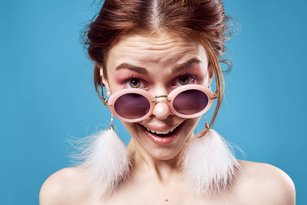 emotional woman wearing sunglasses fluffy earrings jewelry close-up blue background - Photo, Image