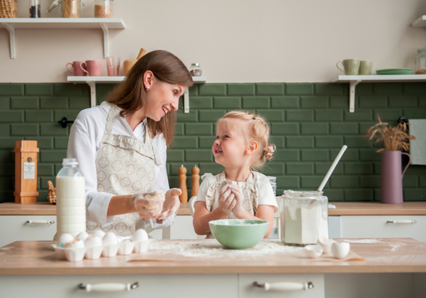 Boldog anya és a kislánya együtt gyúrnak tésztát otthon a konyhában. Kislány segít anya főzni a konyhában - Fotó, kép