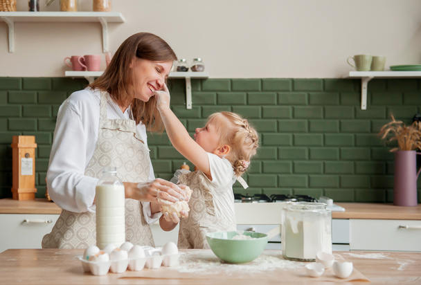 Boldog anya és a kislánya együtt gyúrnak tésztát otthon a konyhában. Kislány segít anya főzni a konyhában - Fotó, kép