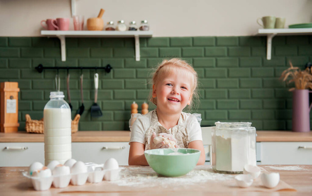 Little happy girl prepares dough in the kitchen. Beautiful child is cooking in the kitchen - Foto, Imagen