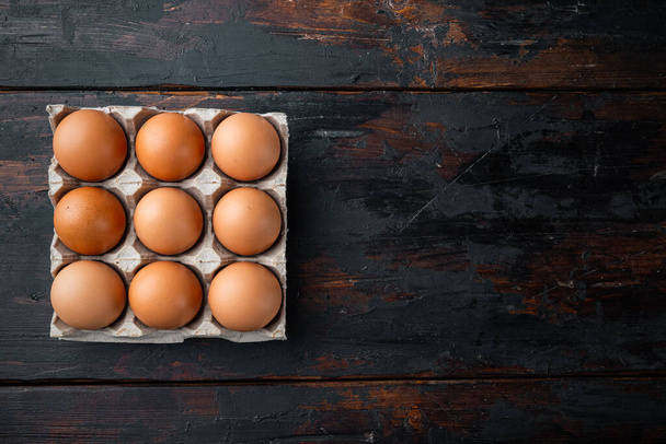 Brown eggs in carton box tray set, on old dark  wooden table background, top view flat lay , with space for text copyspace - 写真・画像
