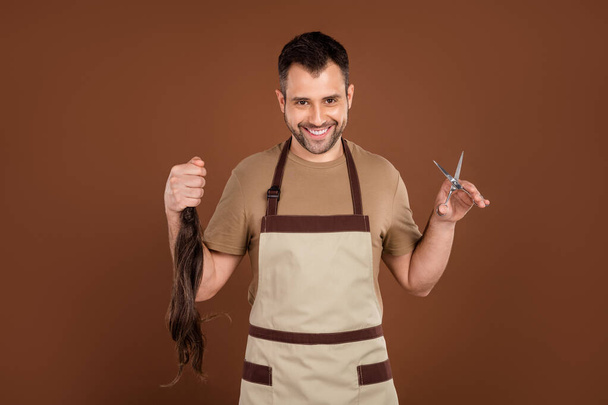 Photo of funny charming young guy dressed beige uniform smiling cutting ponytail isolated brown color background - Φωτογραφία, εικόνα