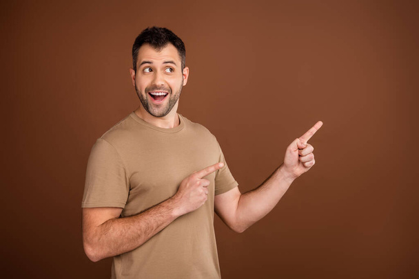 Photo of impressed cute young gentleman wear beige t-shirt pointing looking empty space smiling isolated brown color background - Fotografie, Obrázek
