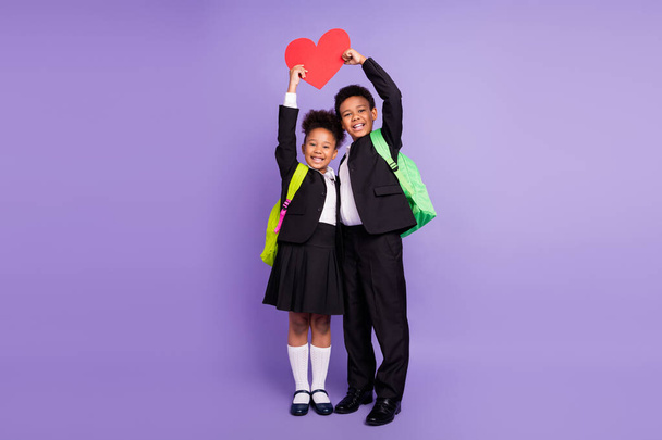 Photo of two romantic african kids hold heart card show feelings wear bag uniform isolated purple color background - Foto, Bild
