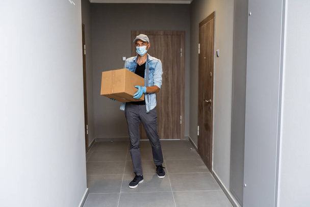 Házhozszállítás bevásárlókocsi férfi kesztyűben és védőmaszkban csomagokat szállít az ajtónál - Fotó, kép