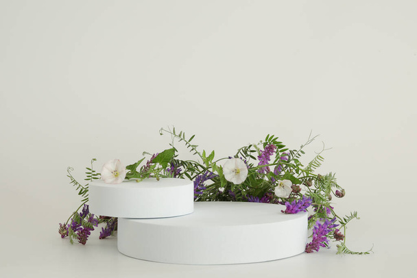 Λευκό βάθρο στο λευκό φόντο με λουλούδια. Στόμιο για το προϊόν, καλλυντική παρουσίαση. Δημιουργική κοροϊδία. Pedestal ή πλατφόρμα για τα προϊόντα ομορφιάς. - Φωτογραφία, εικόνα