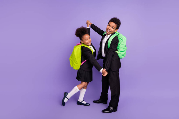 Photo of two african people schoolchildren dance hold hands wear rucksack uniform isolated violet color background - Foto, immagini