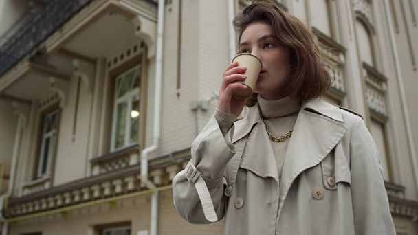 Nuori nainen juo kahvia päästäkseen kadulle. Tyttö nauttii kuuma latte ulkona. - Valokuva, kuva