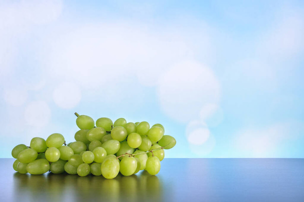 Куча зеленого винограда на столе с отражением на синем фоне боке. Мягкий избирательный фокус. Естественное освещение - Фото, изображение