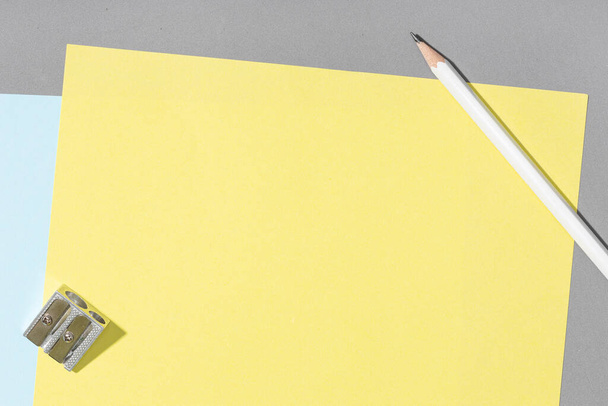 Prázdný žlutý list papíru, bílá tužka a ořezávátko na šedém pozadí. Creative Fock up template flat lay desk - Fotografie, Obrázek