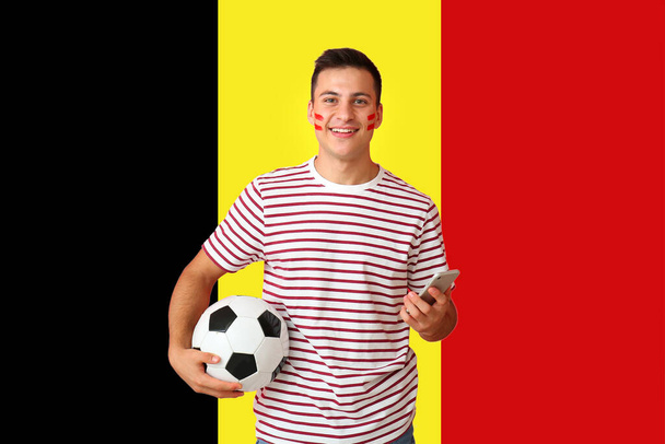 Młody człowiek z piłką nożną i telefonem komórkowym przeciwko belgijskiej fladze - Zdjęcie, obraz