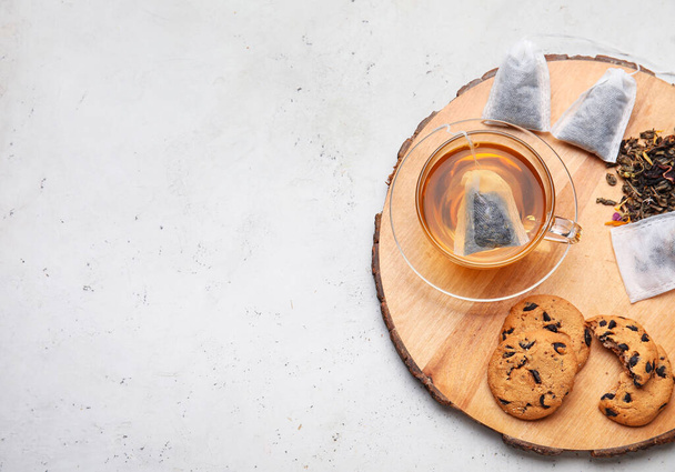 Tazza con tè saporito, biscotti e foglie secche su sfondo chiaro - Foto, immagini