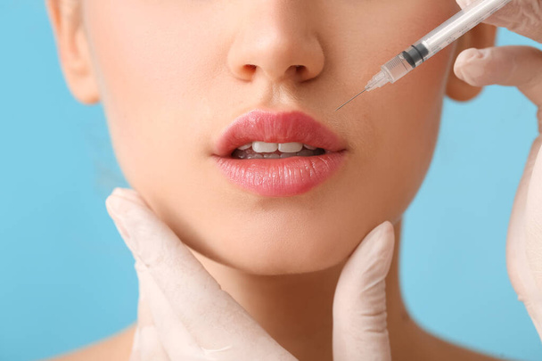 Young woman receiving filler injection in lips against color background, closeup - Photo, Image