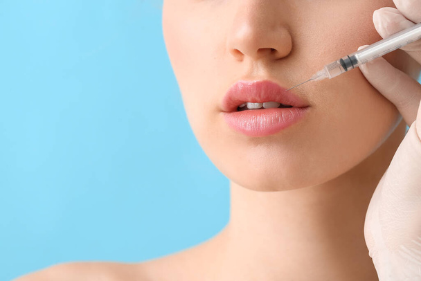 jonge vrouw die vulmiddel injectie in lippen tegen kleur achtergrond, close-up - Foto, afbeelding