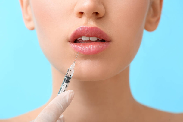 Young woman receiving filler injection in lips against color background, closeup - Foto, immagini