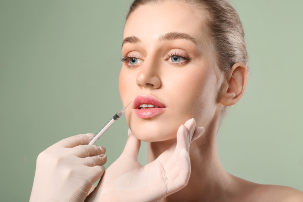 Young woman receiving filler injection in lips against color background - Photo, Image