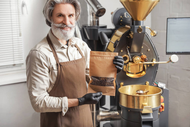 Homem sênior com saco de grãos de café torrados dentro de casa - Foto, Imagem