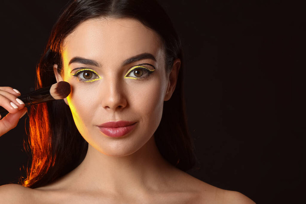 Beautiful young woman with makeup brush on dark background - Valokuva, kuva