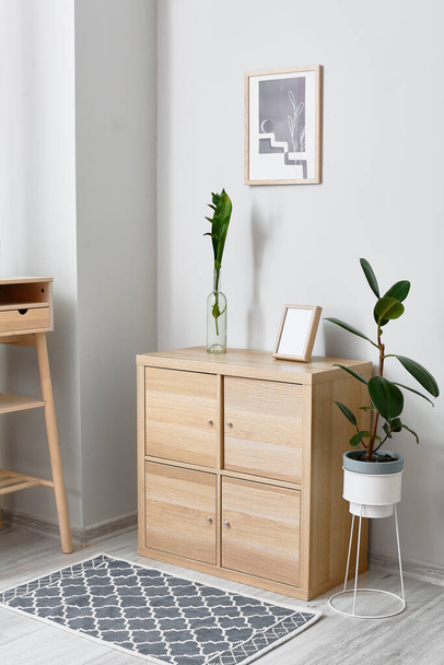 Modern chest of drawers with frame and vase near light wall - Foto, afbeelding