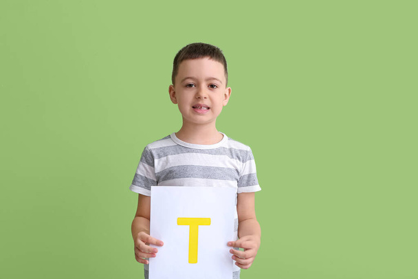 Little boy holding paper sheet with letter T on color background - Foto, imagen