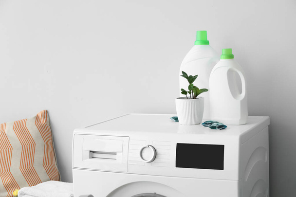 Moderni pesukone pesuaineella ja huonekasvi lähellä kevyttä seinää - Valokuva, kuva