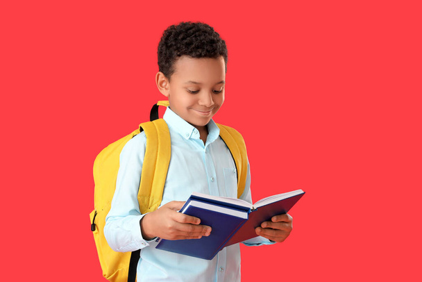 Little African-American schoolboy reading book on color background - Foto, Bild