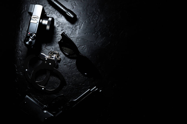 Black gun, flashlight, glasses, camera and Police metal real handcuffs lie on the black background. Private detective work. Searching information. Crime and robbery, prison concept. - Photo, Image