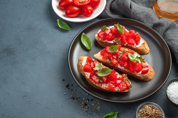 Traditional bruschetta with tomatoes, basil and cream cheese on a dark background. Side view. Italian appetizer. - Foto, Imagem