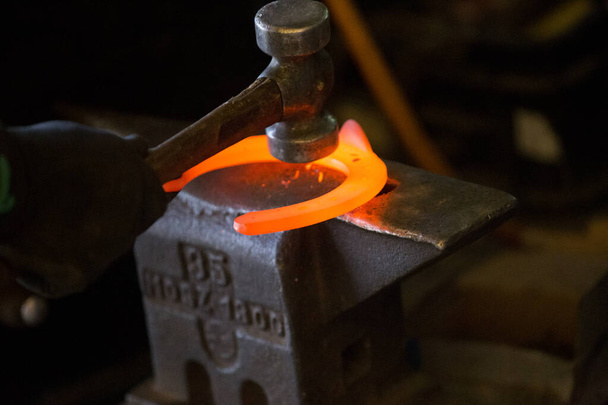 Hard work in the smithy on the anvil. Hammering glowing steel horse shoe. Blacksmith forges a hot horseshoe - Photo, Image
