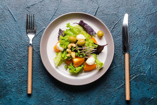 Plate with tasty fresh salad and cutlery on dark background - 写真・画像