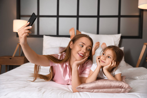 Young woman and her little daughter taking selfie in bedroom - Фото, изображение