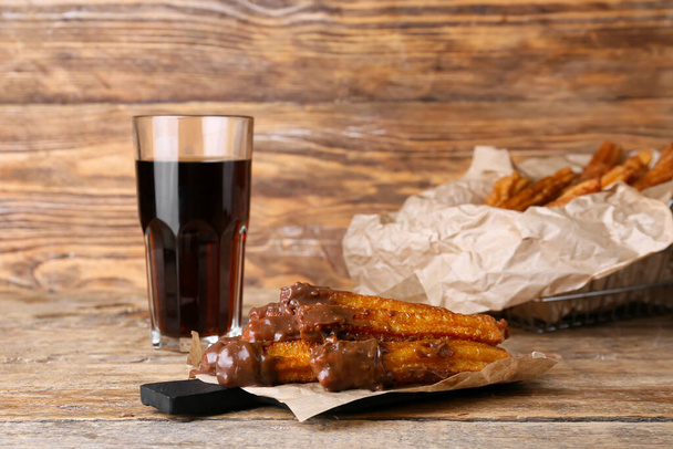 Tasty churros with glass of cola on wooden background - Photo, image