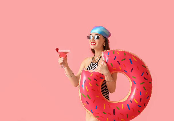 Όμορφη νεαρή γυναίκα με κοκτέιλ και το δαχτυλίδι κολύμπι στο φόντο χρώμα - Φωτογραφία, εικόνα