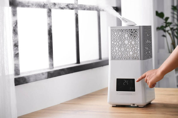 Woman switching on modern humidifier in room - Photo, Image