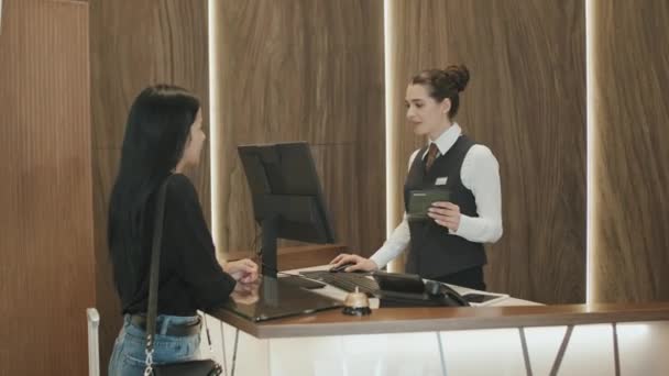 Uma foto média de uma jovem a fazer o check-in no hotel. Recepcionista feminina inserindo informações de passaporte do cliente no computador para reserva de quarto - Filmagem, Vídeo