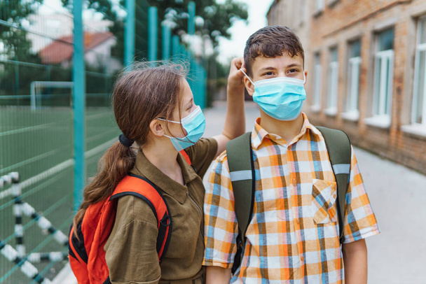 školák a školačka pózují na cestě do školy, na tvářích mají ochrannou masku od koronavirové infekce, vzdělání a zpátky do školy - Fotografie, Obrázek