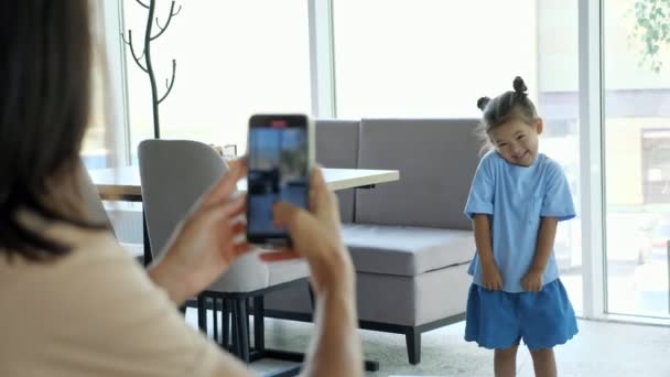 Young woman holds smartphone and makes photo of daughter - Footage, Video