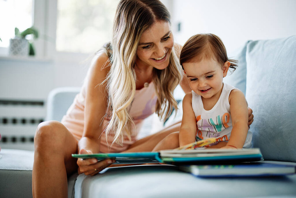 Eine junge Mutter bringt ihrem kleinen Mädchen das Lesen bei. - Foto, Bild