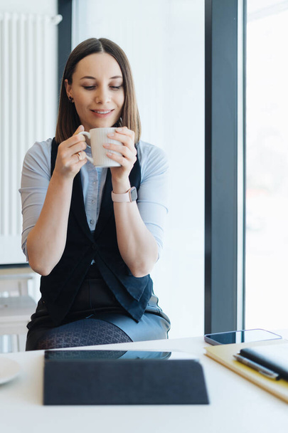 Portret van een jonge vrouw die koffie drinkt aan tafel met tablet in café - Foto, afbeelding