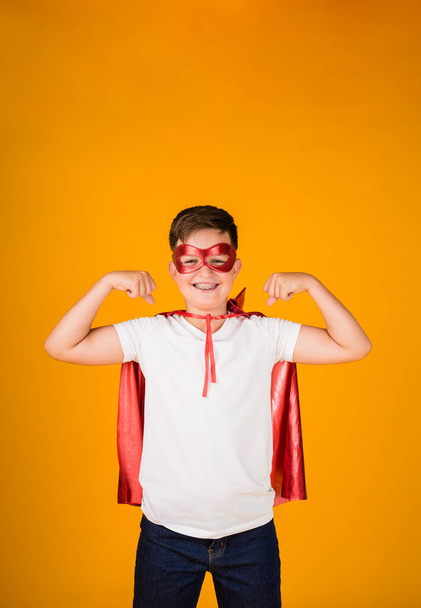 a boy in a hero costume and a mask shows strength on a yellow background with a place for text - 写真・画像