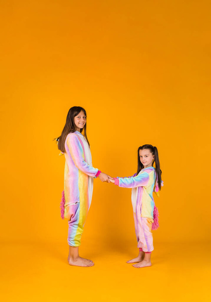 twee vriendinnen in pluche pyjama staan op een gele achtergrond met een plek voor tekst - Foto, afbeelding