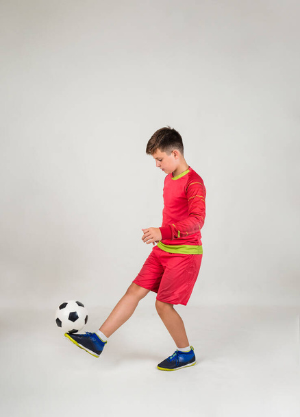 赤いサッカーのユニフォームを着た少年が白い背景にボールをプレーし - 写真・画像