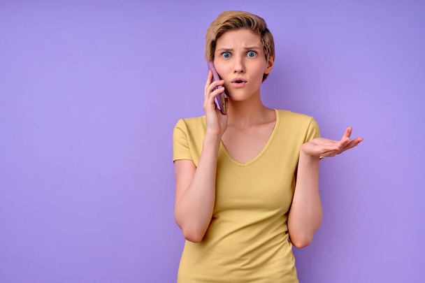 Clueless Caucasian woman talk on phone shrugs shoulders with hesitation, doubtful situation - 写真・画像