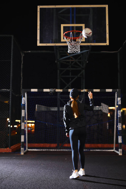 Beautiful Energetic Fitness Woman in Fenced Outdoor Basketball Court. At Night - Foto, Imagen