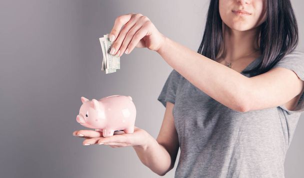 young woman puts a dollar bill in a piggy bank - Valokuva, kuva